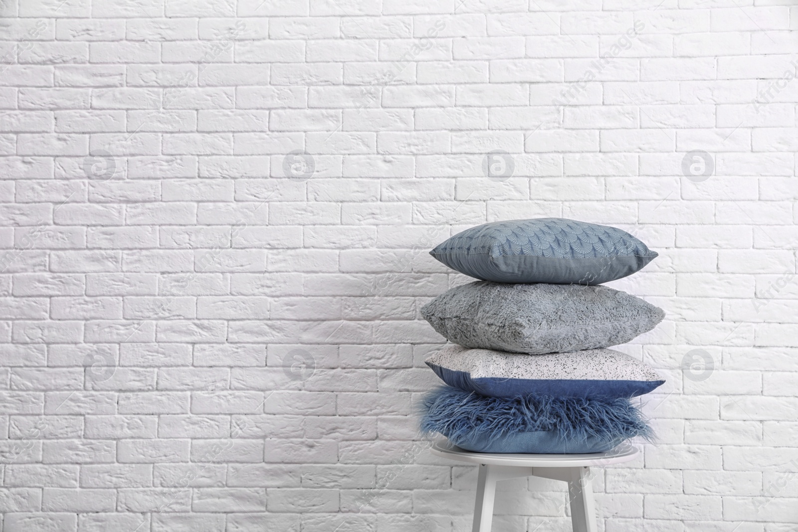 Photo of Many different pillows on chair near brick wall with space for text