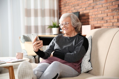 Photo of Elderly woman using smartphone on sofa in living room