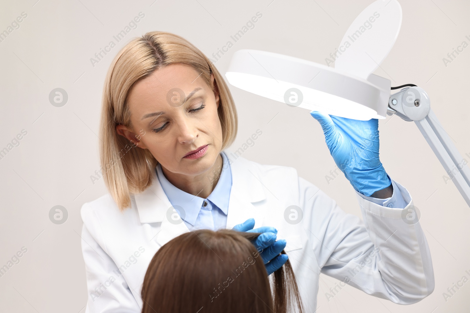 Photo of Trichologist examining patient`s hair under lamp in clinic