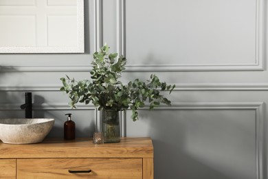 Photo of Stylish vessel sink and eucalyptus branches on bathroom vanity near grey wall, space for text. Interior design
