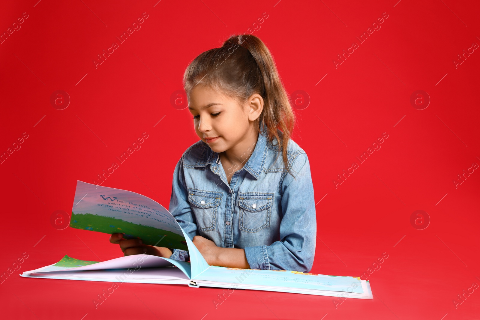 Photo of Cute little girl reading book on red background