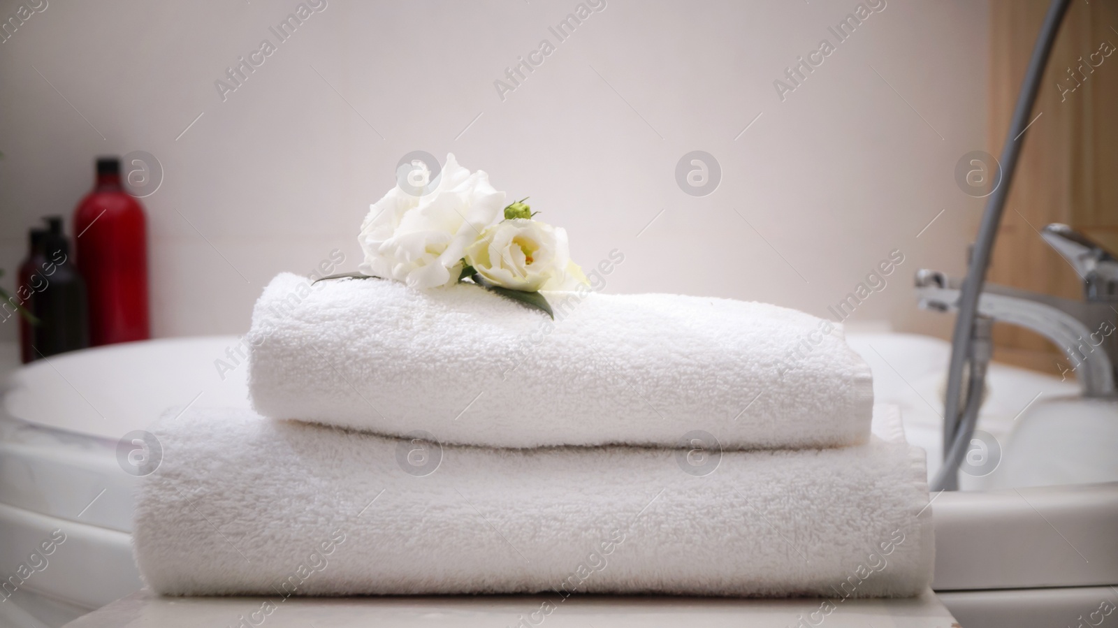 Photo of Stacked bath towels and beautiful flowers on table in bathroom