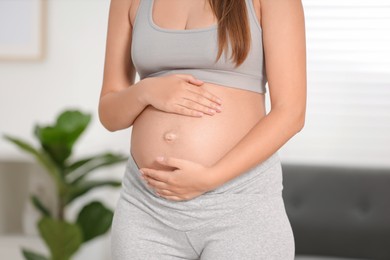 Photo of Pregnant woman standing near sofa at home, closeup