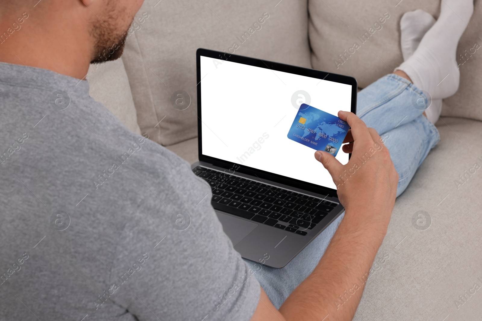 Photo of Man with credit card using laptop for online shopping on sofa, closeup