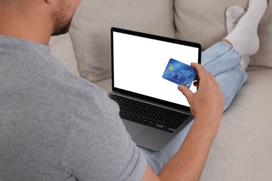 Photo of Man with credit card using laptop for online shopping on sofa, closeup