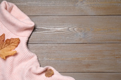 Pink sweater and autumn leaves on wooden background, top view. Space for text