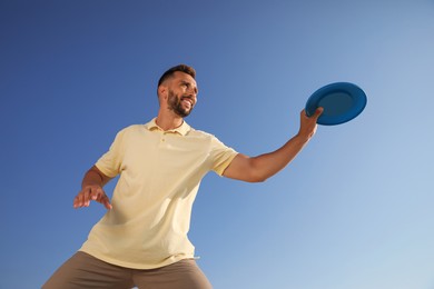 Photo of Happy man catching flying disk against blue sky on sunny day, low angle view