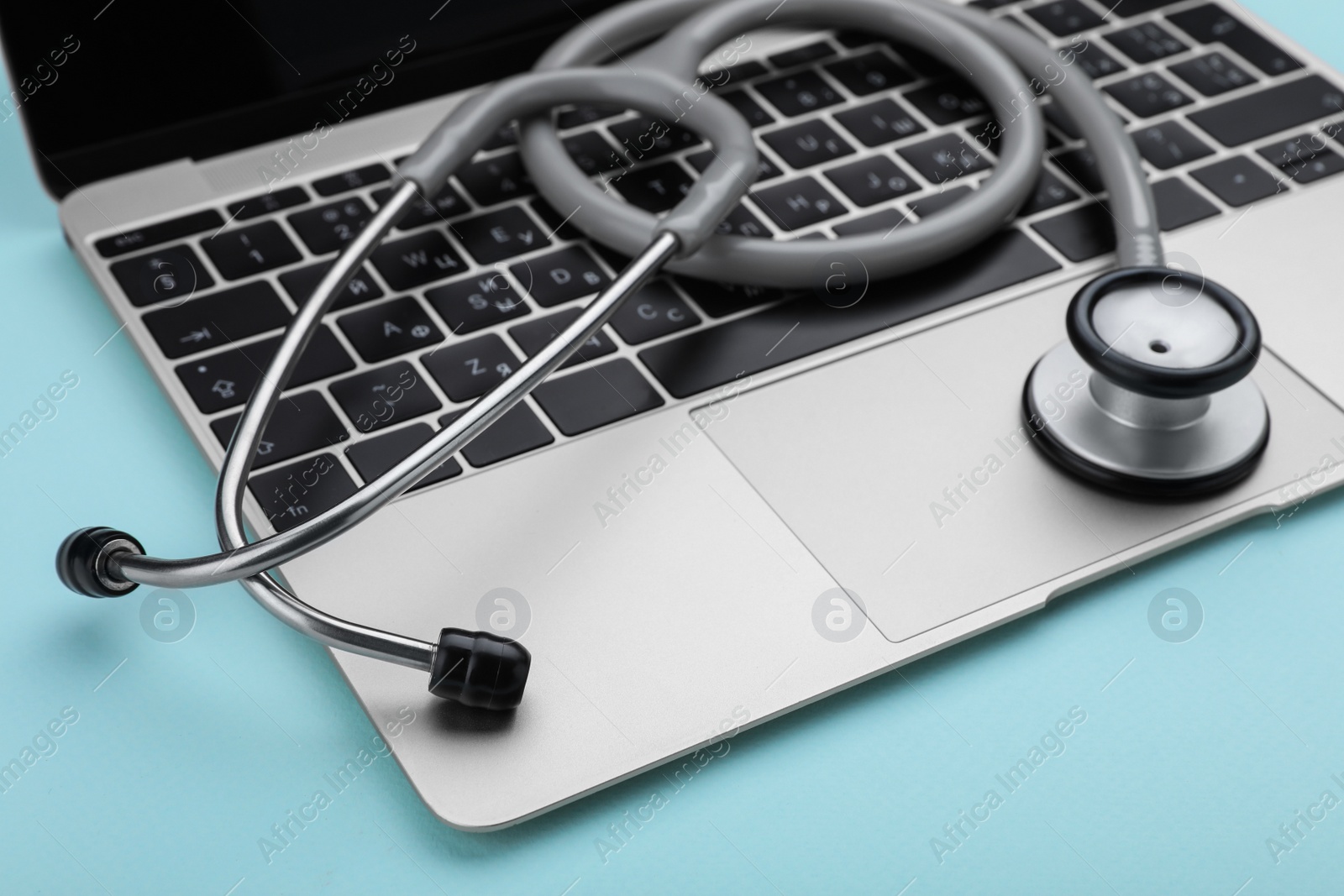 Photo of Laptop and stethoscope on turquoise background, closeup