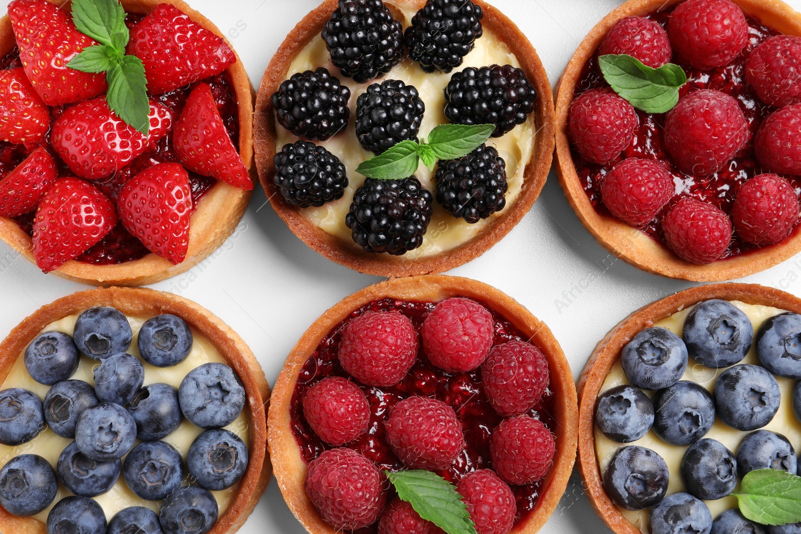 Photo of Tartlets with different fresh berries on white table, flat lay. Delicious dessert