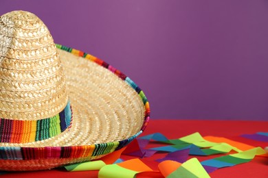 Photo of Mexican sombrero hat on red table, closeup. Space for text