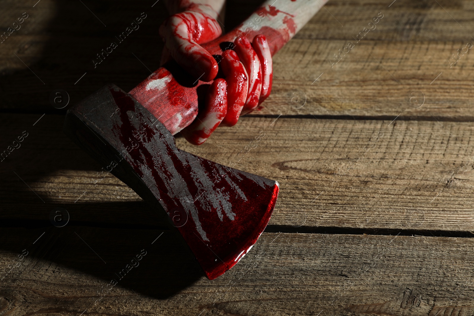 Photo of Man holding bloody axe on wooden surface, closeup