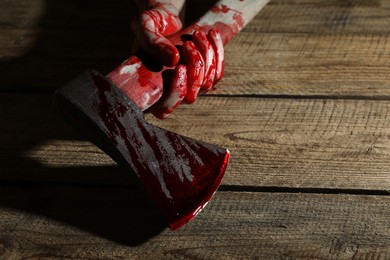 Photo of Man holding bloody axe on wooden surface, closeup