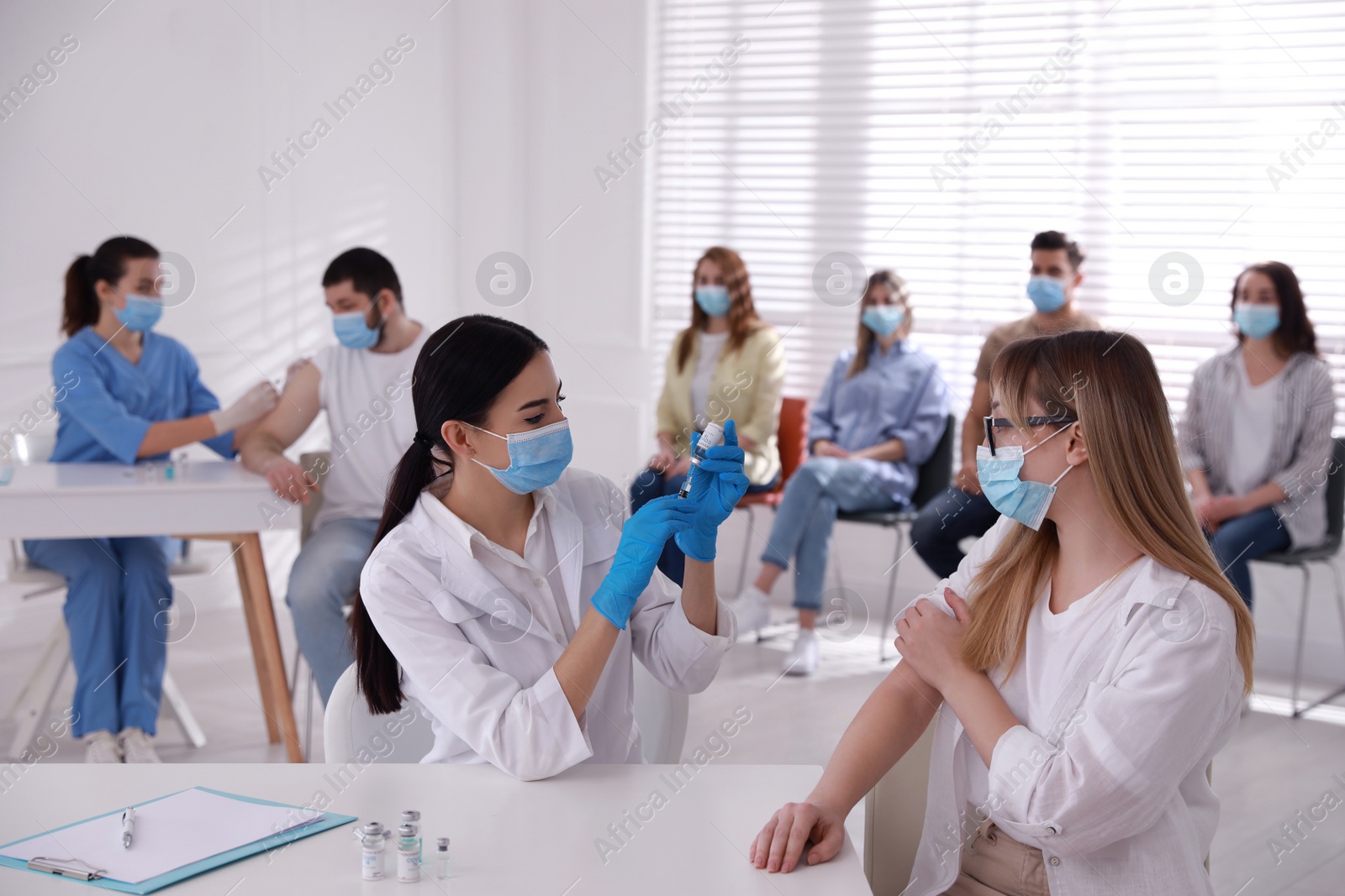 Photo of Doctor giving injection to patient while other waiting in line at hospital. Vaccination campaign