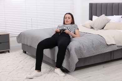 Photo of Woman trying to put on tight jeans on bed at home