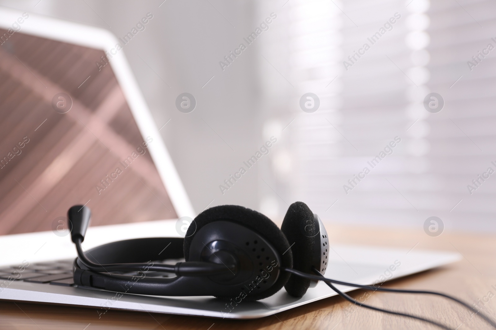 Photo of Modern laptop with headset on wooden table in office, space for text. Hotline service