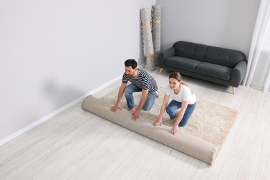 Photo of Smiling couple unrolling carpet on floor in room