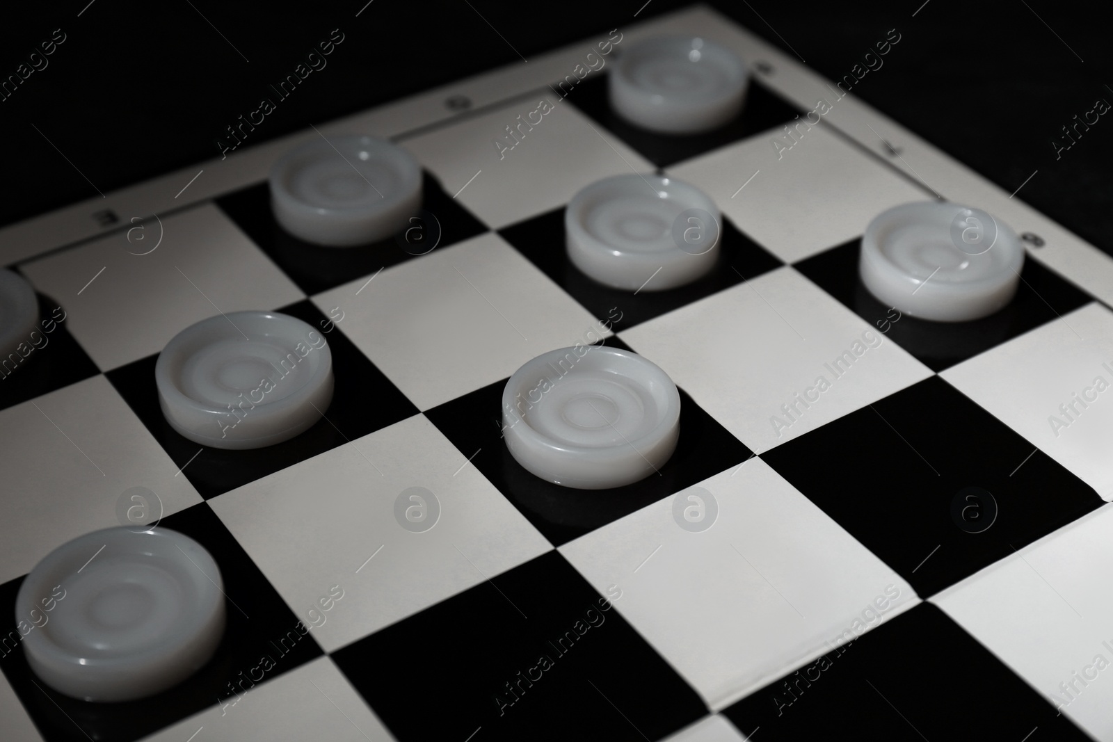 Photo of Checkerboard with game pieces on dark background, closeup