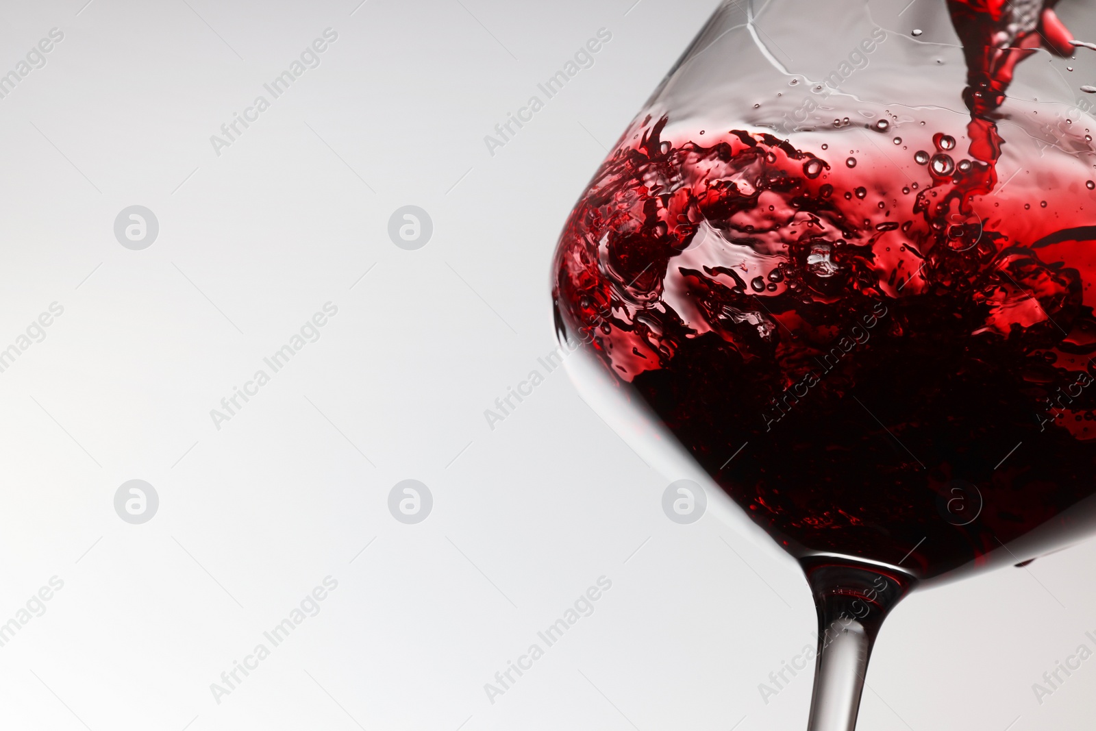 Photo of Pouring tasty red wine in glass on white background, closeup. Space for text