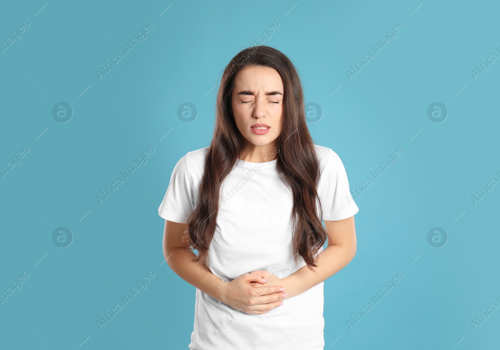 Photo of Young woman suffering from stomach ache on light blue background. Food poisoning