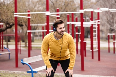 Young man with headphones listening to music and exercising on sports ground