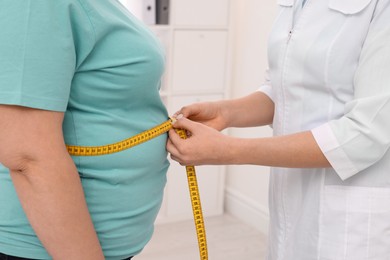 Photo of Nutritionist measuring overweight woman's waist with tape in clinic, closeup