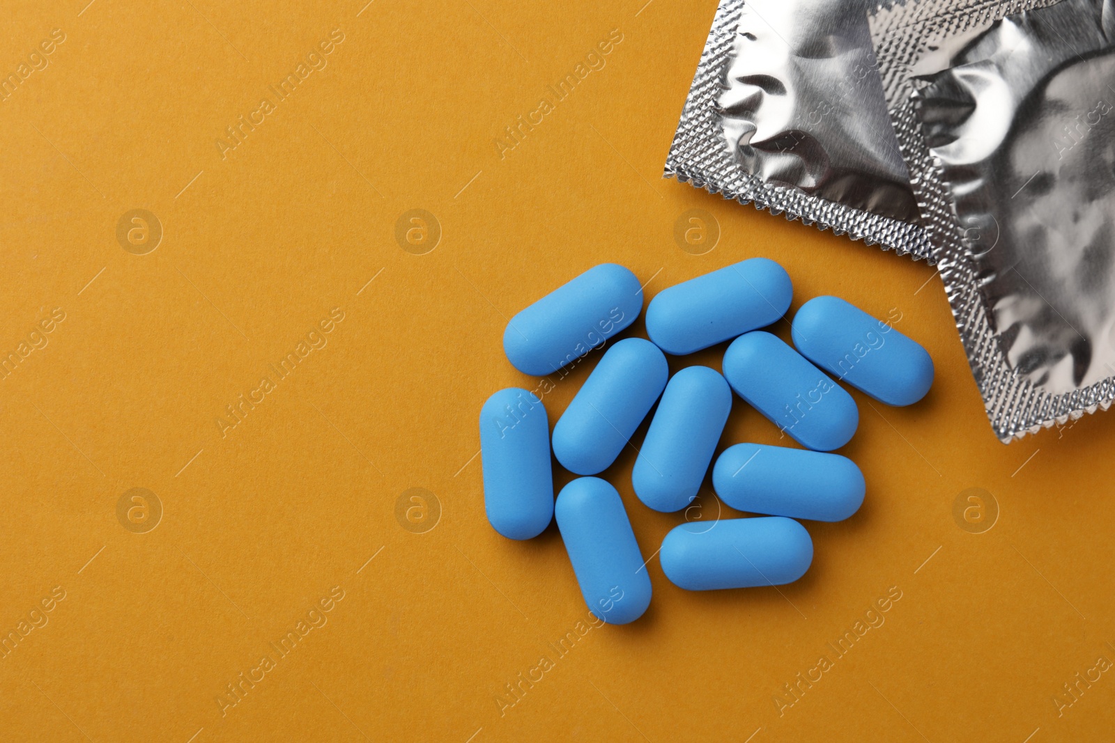 Photo of Pills and condoms on orange background, flat lay with space for text. Potency problem