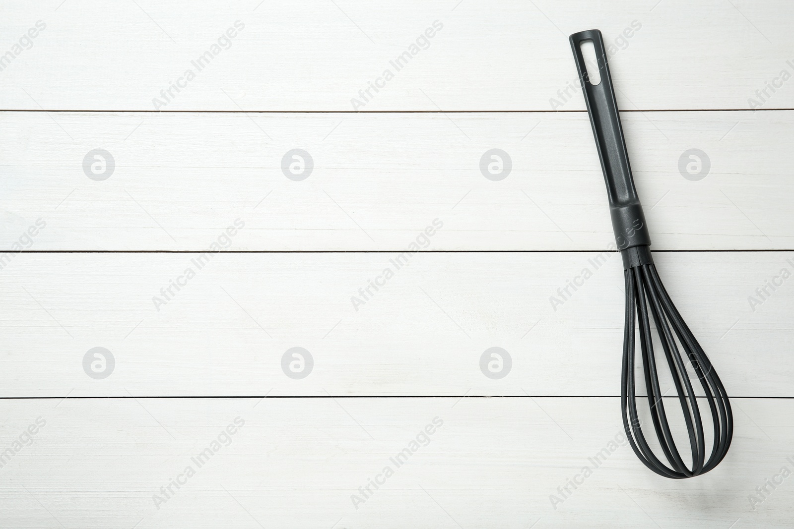 Photo of Plastic whisk on white wooden table, top view. Space for text