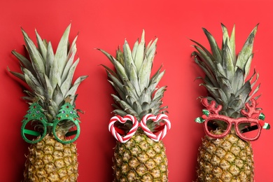 Photo of Pineapples with party glasses on red background, flat lay. Creative concept