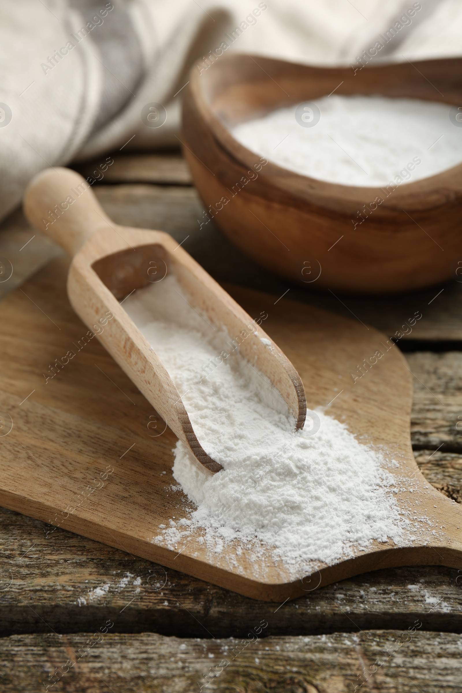 Photo of Baking powder in scoop and bowl on wooden table, closeup