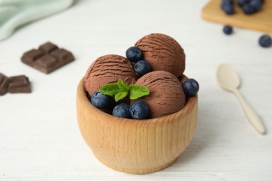 Wooden bowl of chocolate ice cream and blueberries on white table