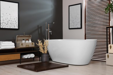 Photo of Stylish bathroom interior with ceramic tub, towels and cosmetic products