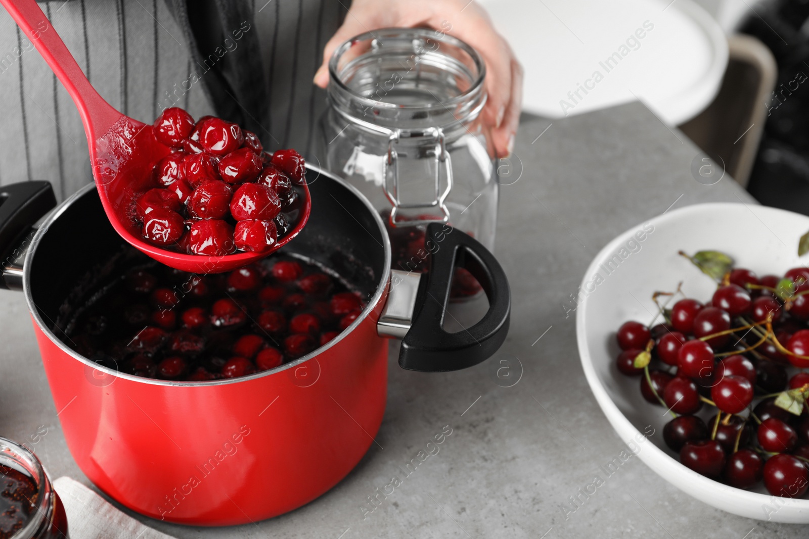 Photo of Woman making pickled cherries at table indoors, closeup