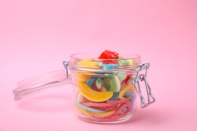 Photo of Tasty jelly candies in open jar on pink background, closeup