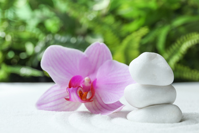 Photo of Stack of white stones and beautiful flower on sand against blurred green background. Zen, meditation, harmony