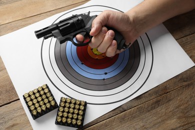 Man with handgun, shooting target and bullets at wooden table, closeup