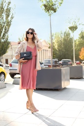 Photo of Young woman in sunglasses with stylish black bag on city street