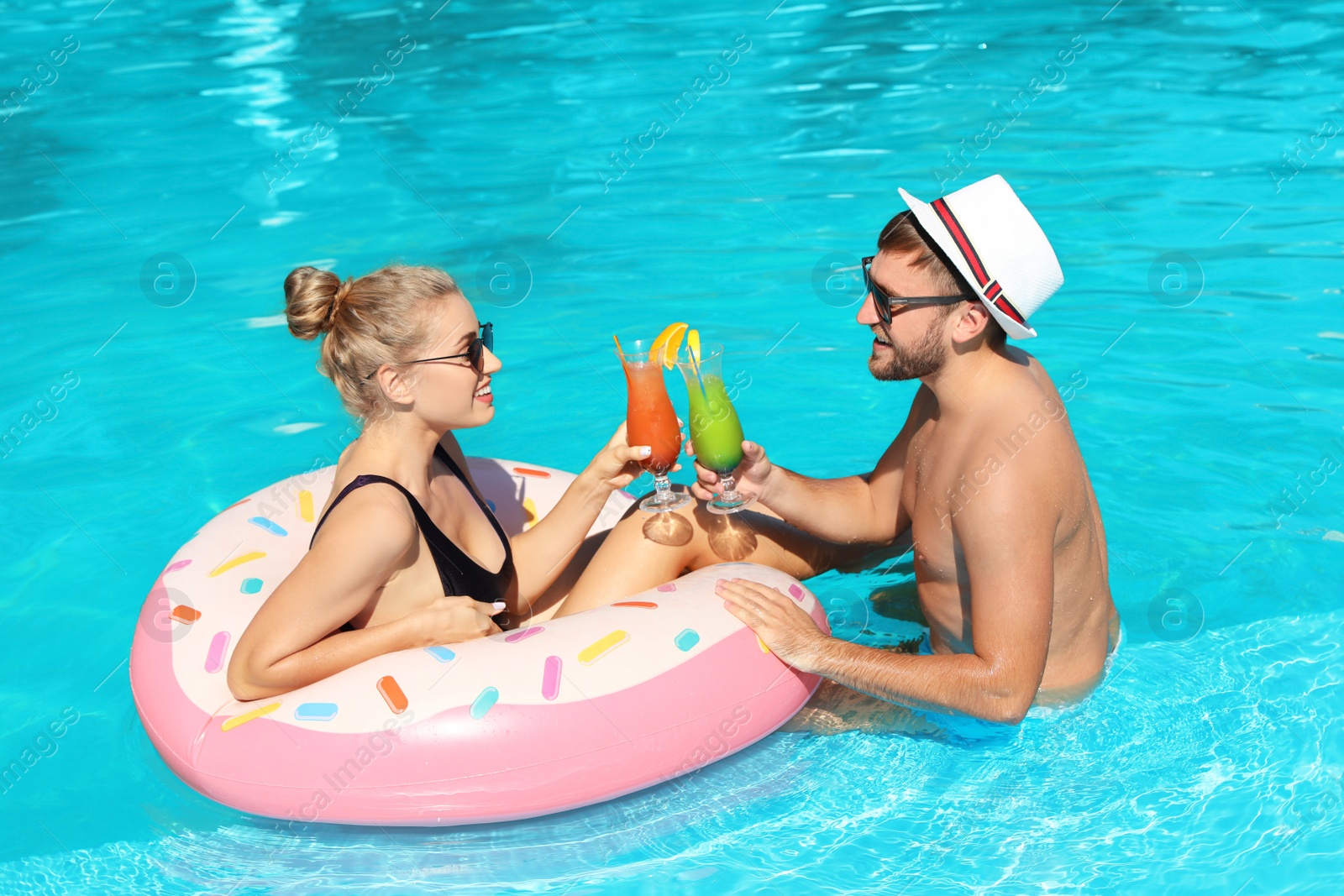 Photo of Young couple with refreshing cocktails and inflatable ring in swimming pool