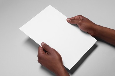 Photo of African American man holding sheet of paper on white background, closeup. Mockup for design