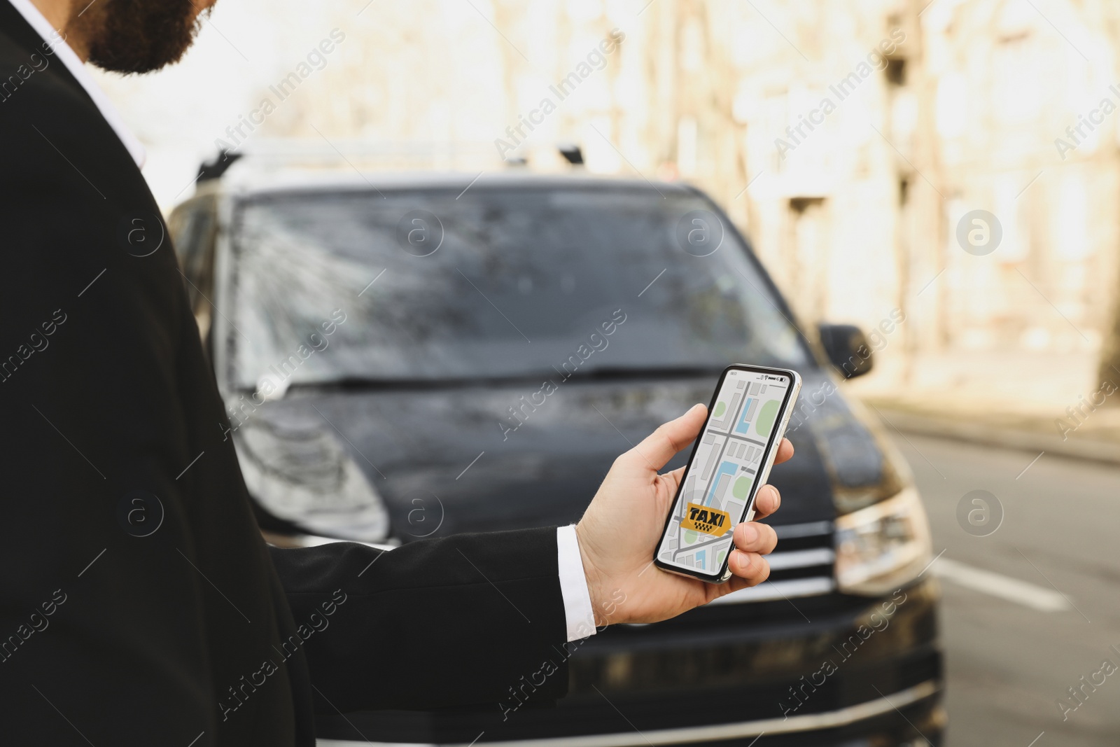 Photo of Businessman ordering taxi with smartphone on city street, closeup