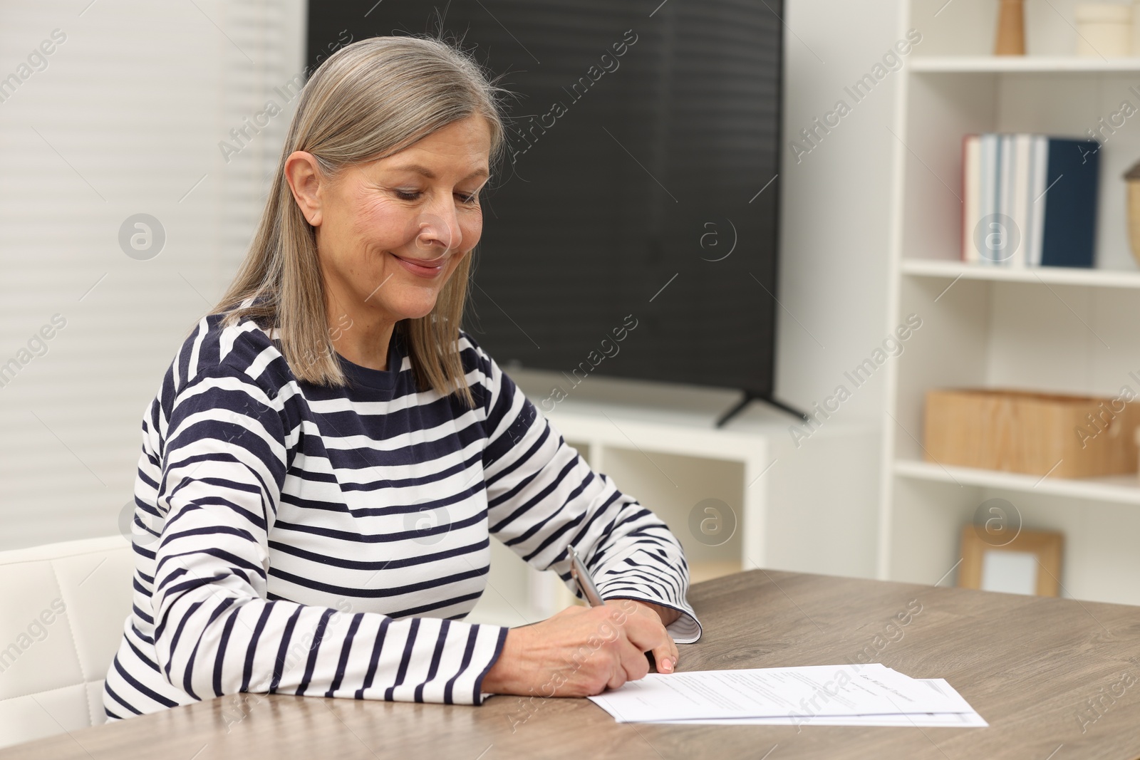 Photo of Senior woman signing Last Will and Testament at wooden table indoors. Space for text