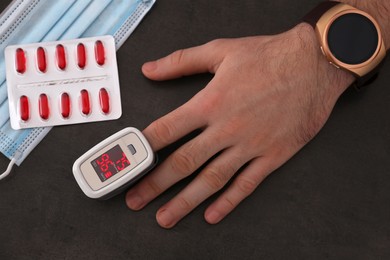 Man measuring oxygen level with modern fingertip pulse oximeter at grey table, top view