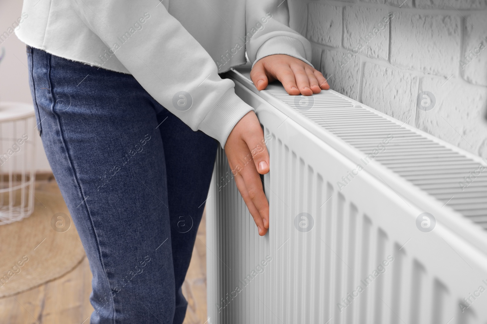 Photo of Girl warming hands on heating radiator indoors, closeup