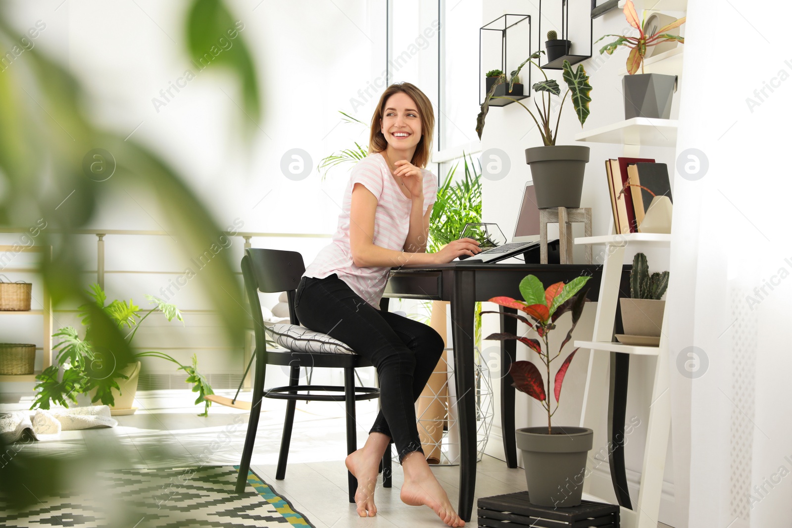 Photo of Young woman using laptop at home, space for text. Trendy room interior with plants