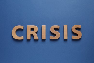 Photo of Word Crisis made of wooden letters on blue background, flat lay