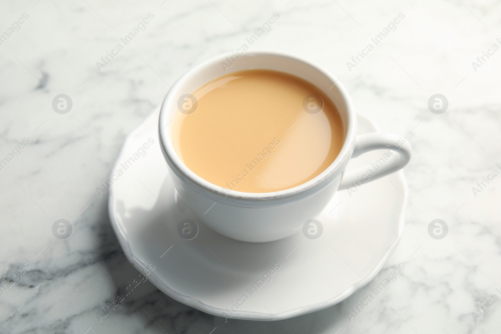 Photo of Cup with black tea and milk on marble table