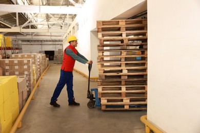 Image of Worker moving wooden pallets with manual forklift in warehouse