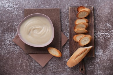 Bowl with tasty creamy soup of parsnip and fried baguette on brown textured table, flat lay