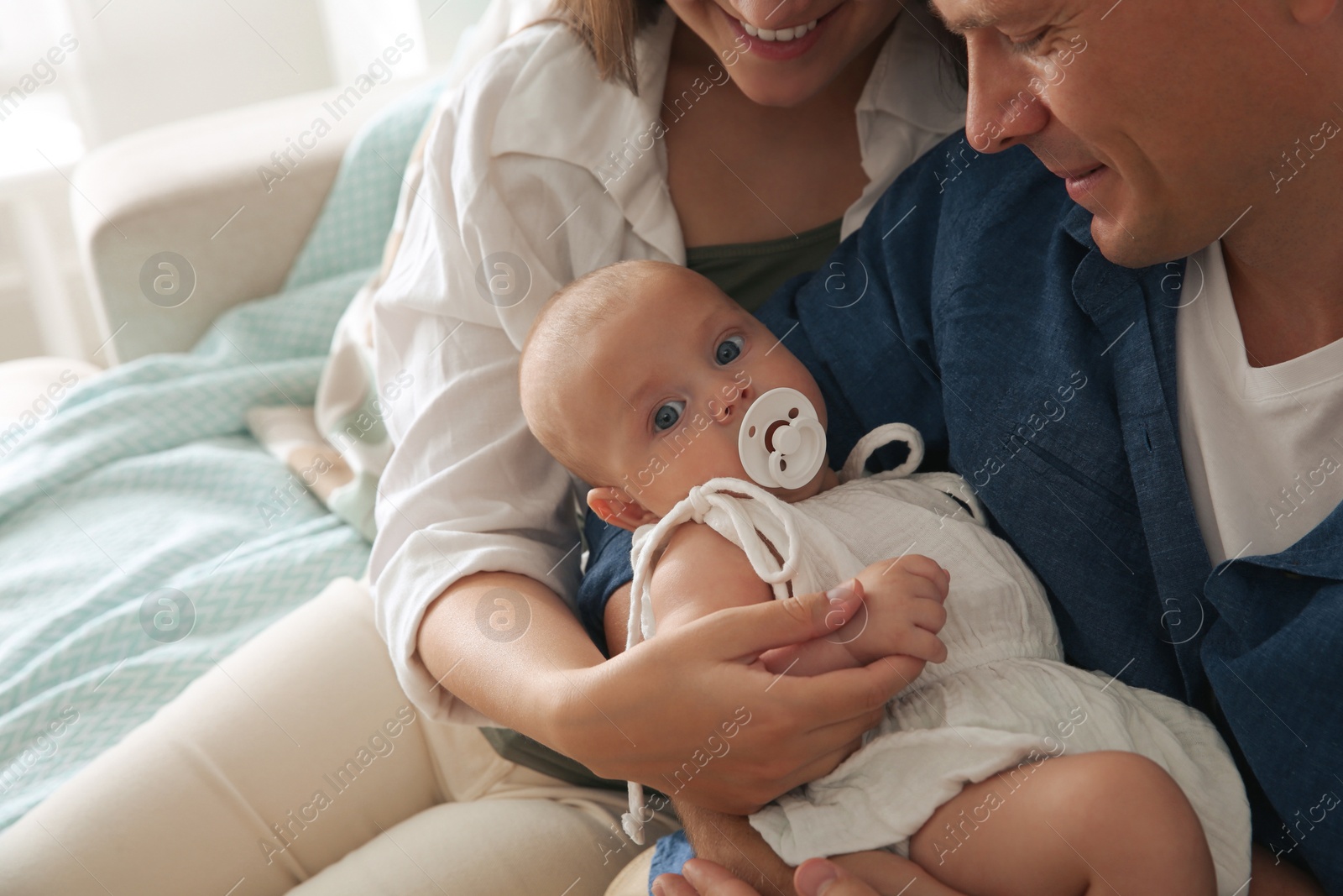 Photo of Happy couple holding their cute little baby with pacifier at home, closeup