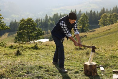 Photo of Handsome man with axe cutting firewood on hill