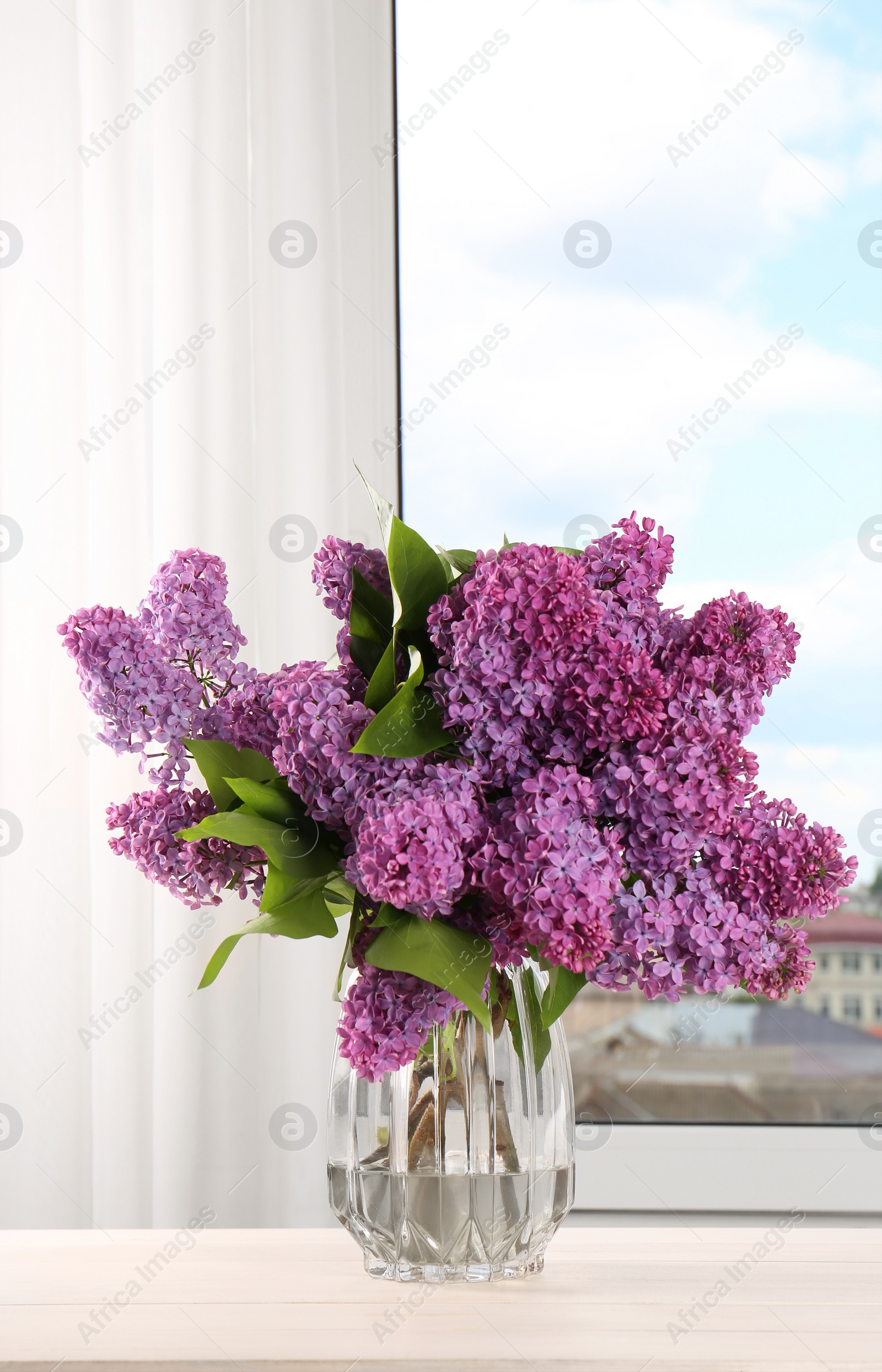 Photo of Beautiful lilac flowers in vase on white wooden table indoors